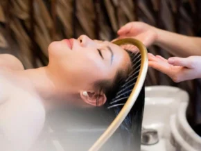 Relaxing Hair Spa & Body Massage Treatment - Rosie's Magical Spa A woman lies with her eyes closed, receiving a soothing hair spa treatment from a therapist. Her hair is wet and being massaged, indicating a relaxing salon or spa experience.