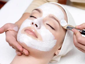 A client receiving a luxurious facial care treatment at Rosie's Magical Spa, with an esthetician applying a white nourishing mask with a brush.