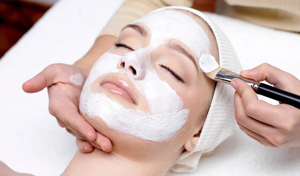 A client receiving a luxurious facial care treatment at Rosie's Magical Spa, with an esthetician applying a white nourishing mask with a brush.