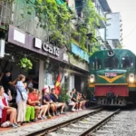 Tourists watching a train pass by closely at a cafe along Hanoi Train Street, capturing the unique cultural experience in Vietnam's Old Quarter.